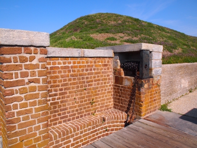 [Rolled chain inside a brick housing. No handle on the wooden chain roll. Part of wooden drawbrige seen at bottom.]